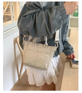 Detail view of cream-white nylon tote bag with wide strap and spacious front pocket
