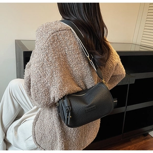 Détail d'un sac bandoulière en cuir grainé noir avec large sangle rayée sur modèle