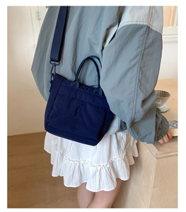 Detail of navy blue nylon mini tote bag worn crossbody in a lifestyle coffee shop setting