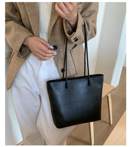 Detail of a minimalist black faux leather tote bag showing smooth texture and clean stitching