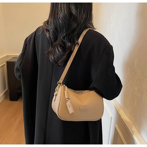 Détail d'un sac demi-lune en cuir beige texturé montrant la plaque en métal fashion