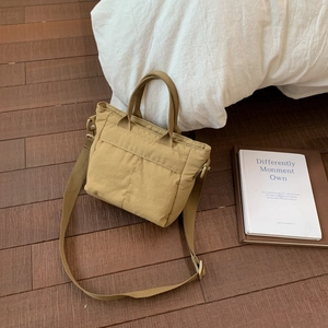 Detail view of khaki nylon tote bag with reinforced stitching and adjustable strap on wood floor