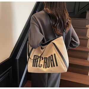 Détail d'un grand sac cabas en toile avec anses en cuir noir porté par un mannequin