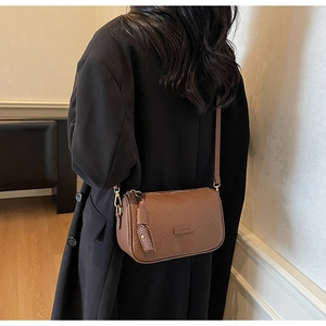 Détail du sac bandoulière en cuir grainé marron avec fermetures éclair dorées sur manteau