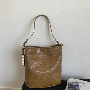Detail of tan woven leather bucket bag featuring vintage bead pendant and metal ring