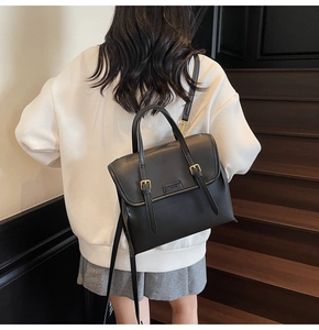 Detail view of the black leather backpack showing matte texture and gold metal buckles