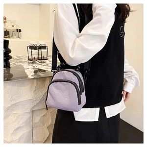 Detail of light purple nylon crossbody bag with zipper compartments and black strap