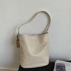 Detail of beige woven bucket bag featuring wood bead charm and premium PU leather texture
