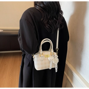 Detail of checkered shoulder bag featuring a gold twist lock and pearl heart pendant