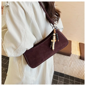 Close-up of burgundy suede shoulder bag with ethnic beaded tassel on a trench coat