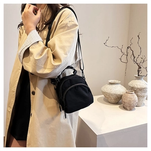 Detailed view of a black mini crossbody shell bag with double zippers and canvas texture