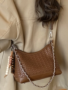 Caramel brown woven crossbody pillow bag with chain strap and bead detail on a model
