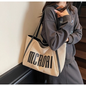 Détail du sac cabas en toile beige avec bordures en cuir noir et broderie de lettres