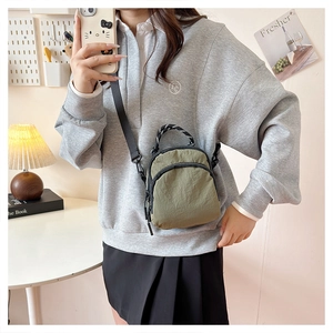 Mirror selfie showing the olive green nylon mini crossbody bag with woven handle details