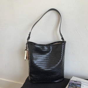 Detail of black woven bucket bag with intricate texture and colorful beaded charm