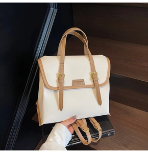 Close-up of retro beige tote bag with brown leather trim and dual metal buckles detail