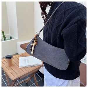 Detail of grey suede hobo bag with unique beaded wooden fringe on dark sweater