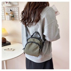 Olive green mini crossbody bag in wrinkled nylon fabric worn by a model in a cozy room