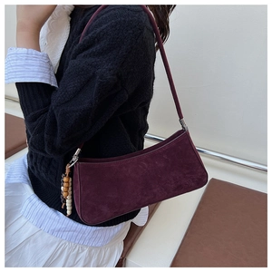 Detail of burgundy suede baguette bag featuring unique wooden bead charm on the side