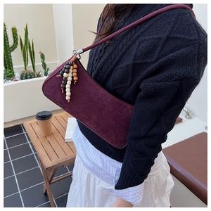 Detail of burgundy suede shoulder bag with retro wooden bead tassel on a side view