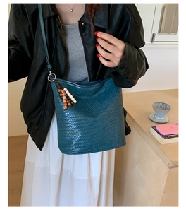 Detailed view of dark blue woven bucket bag with wood bead tassel and adjustable strap