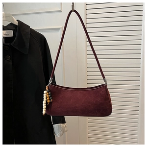 Detail of burgundy suede baguette bag with colorful beaded charm hanging on a white door
