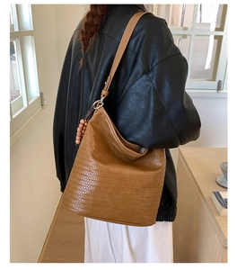 Brown woven bucket bag featuring detailed craftsmanship and a decorative wooden bead charm