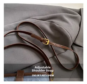 Detail of adjustable brown leather shoulder strap with gold buckle on denim bucket bag
