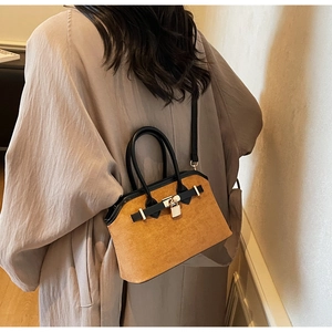 Détail du sac cabas en daim marron porté sur un manteau kaki avec un fermoir métallique