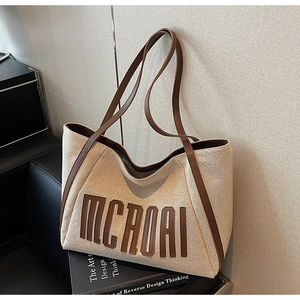 Détail d'un sac cabas en toile beige avec logo en cuir marron et lanières