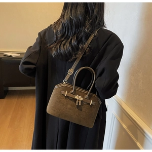 Détail d'un sac cabas en daim marron foncé avec un cadenas doré et une bandoulière fine