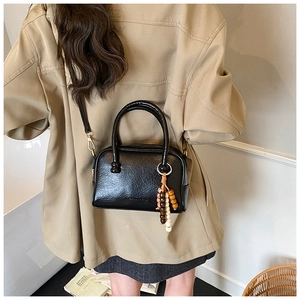 Détail du sac à main en cuir synthétique noir avec texture grainée et charme en bois