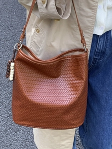 Retro brown woven bucket bag with wood bead charm shown on shoulder outdoors