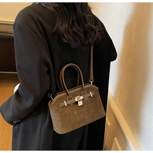 Détail du sac cabas en daim marron mat avec boucle dorée et poignée porté par un mannequin