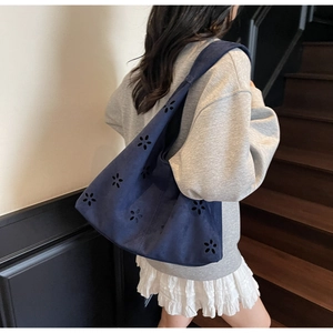 Détail d'un sac hobo bleu marine avec fleurs ajourées porté à l'épaule