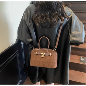 Détail du sac fourre-tout en daim marron avec boucles dorées porté en bandoulière