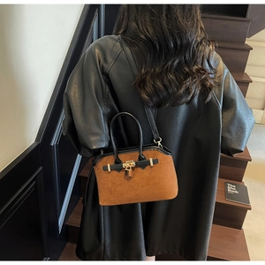 Détail d'un sac à main en daim marron avec bordure en cuir noir et cadenas doré élégant