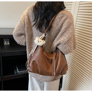 Brown leather crescent tote with pleated base detail and a plush bear charm on the strap