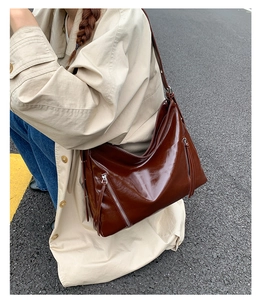 Outdoor view of brown glossy leather shoulder bag with decorative silver zippers