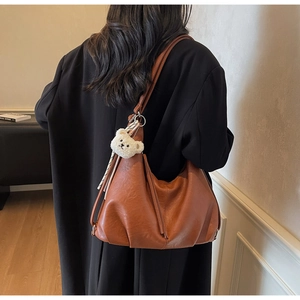 Close-up of brown large tote bag featuring wave-shaped pleats and a plush bear charm