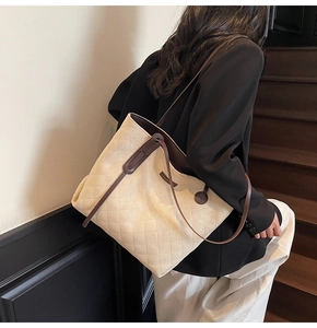 Close-up of quilted tote bag featuring brown leather handles and minimalist side label