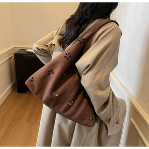 Détail d'un motif floral découpé au laser sur un sac hobo en daim marron porté