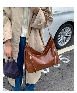 Detail of caramel brown tote bag with oily leather texture and tassel zipper accents