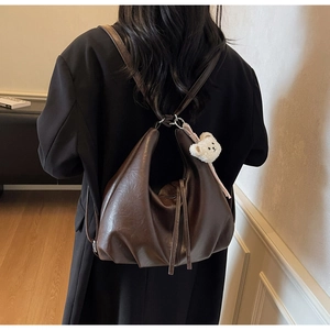Detail view of large dark brown leather tote bag with a white plush bear charm on a model