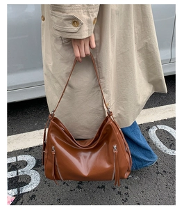 Caramel brown leather hobo bag with silver zippers and long tassels in outdoor street setting