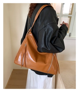 Detailed side view of a large brown leather tote bag with vertical zippers on a model
