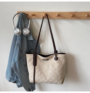 Close-up of quilted tote bag with brown leather straps hanging on a wall rack
