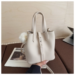 Detail view of cream bucket bag with lychee texture and plush charm in casual setting