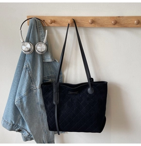 Detail view of black quilted tote bag with suede texture hanging in a lifestyle setting