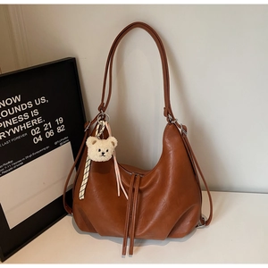 Detail view of caramel brown PU leather bag featuring pleated bottom and plush bear charm